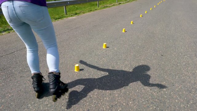 A woman in jeans learns to skate on roller skates. She does special exercises while driving through the chips.