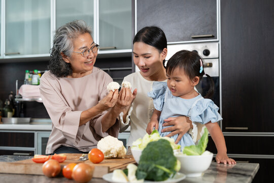 Generations of Culinary Bonds: An elderly woman, her daughter, and her granddaughter share a tender moment in a domestic kitchen, working together to prepare a meal.