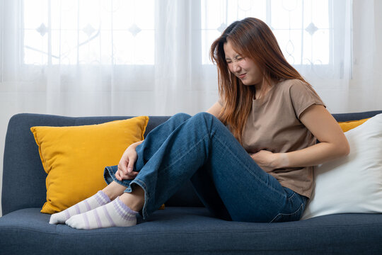 Internal Discomfort: A person, experiencing stomach discomfort, sits on a comfortable sofa, their body language conveying distress and pain.