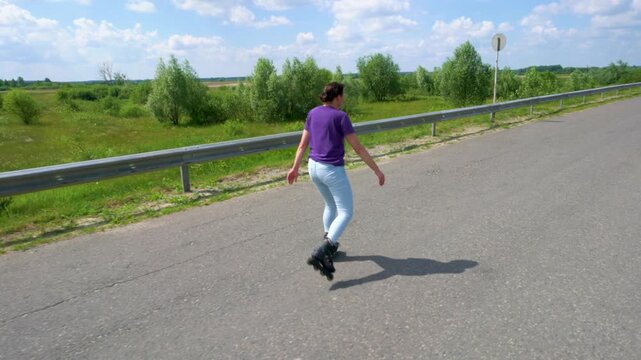 An adult woman in jeans is riding on roller skates along an asphalt road.