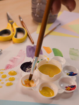 Close-up of a Child Dipping a Paintbrush into Yellow Paint Palette