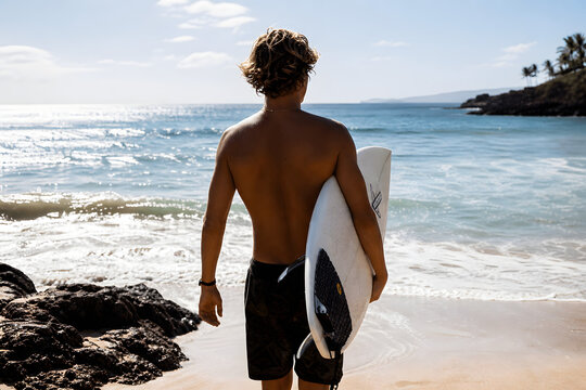 Back view surfer holding board on sunny beach