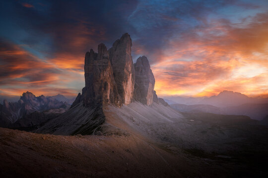 View of the jagged Tre Cime di Lavaredo peaks under a sunset sky with orange clouds and rocky mountain slopes in Auronzo di Cadore, Veneto, Italy.