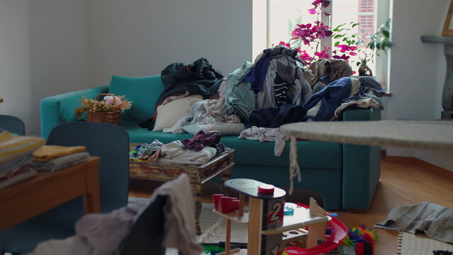 Massive stack of unfolded clothes covering living room sofa and spilling onto cushions highlighting domestic overload and never ending household responsibilities