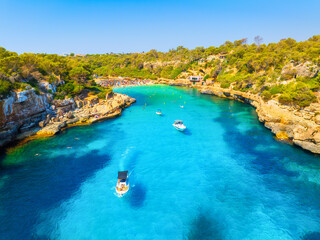 Obraz premium Aerial view of a boat in a Llombards beach, Mallorca, Spain. Summer vacation concept with azure Mediterranean water, scenic coastline and drone landscape. Travel and relaxation in the sun.