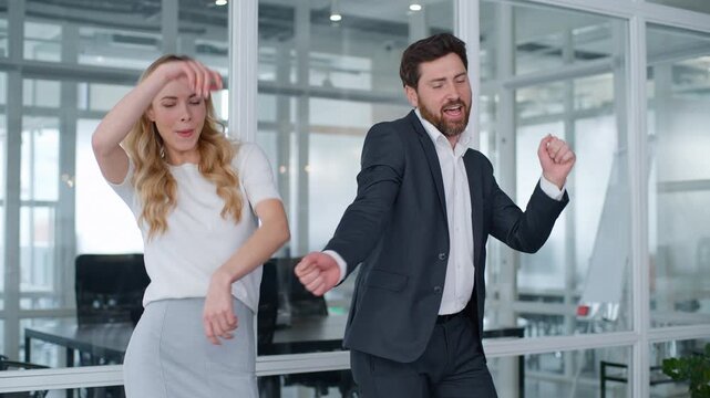 Two funny silly business partners woman and man dancing singing at office workplace carefree cheerful humorous Caucasian middle-aged businessman with businesswoman dance sing moving to music fooling