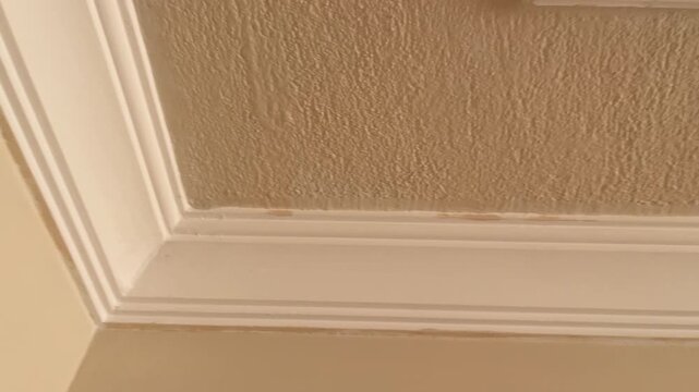 White classic crown molding detail separating a smooth beige wall from a textured ceiling in a modern house interior showing architectural home improvement finishes