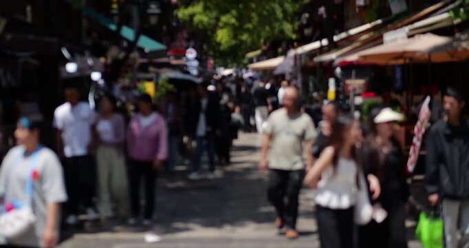 Blurred view of diverse flow of pedestrians walking leisurely along shopping street in Wuhua District, downtown Kunming. High contrast shot captures relaxed atmosphere under bright sunny daylight