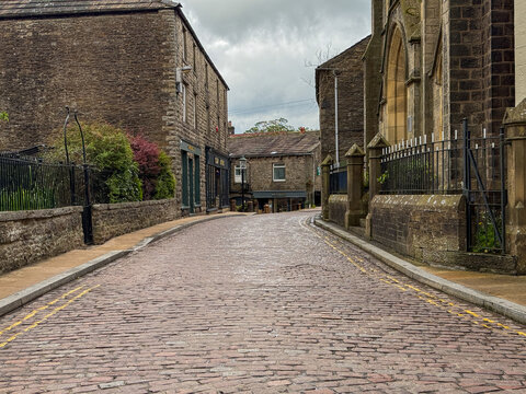 View of a traditional cobbled street lined with historic stone buildings under a cloudy sky in Hawes, England, United Kingdom.