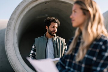 Fototapeta premium Construction workers inspecting large concrete pipe at a site with male and female engineers for industrial background and teamwork banner design