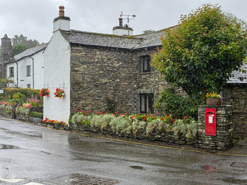 View of traditional stone cottages with flower boxes and a red post box along a wet street in Hawes, England, United Kingdom.