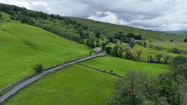 View of the rolling green hills and traditional dry stone walls along a winding country road in Hawes, England, United Kingdom.