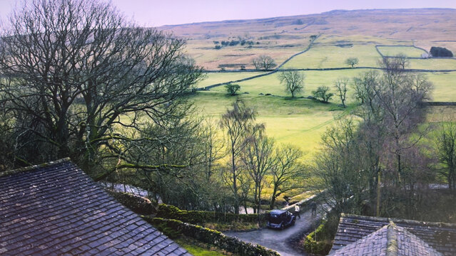 View of the rolling green hills and stone walls of the Yorkshire Dales with a vintage car and people walking on a narrow road Hawes, England, United Kingdom.