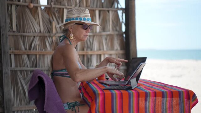 Mature woman shows emotion while having video chat on computer, tablet, and phone on a tropical beach during her vacation time.