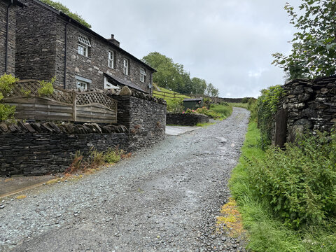 View of traditional stone cottages and a gravel path lined with dry stone walls under an overcast sky in Hawes, England, United Kingdom.