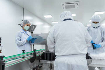 Naklejka premium Cleanroom workers check products on automated production li. Quality control inspector and factory workers operating automated packaging machinery in a sterile pharmaceutical manufacturing facility.