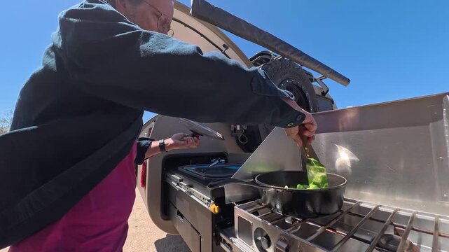 Mature man prepares food on stove while camping with a teardrop trailer at the beach in Baja California, Mexico.