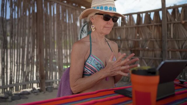 Happy mature woman using computer and tablet on beach under sun during her vacation in a tropical location.