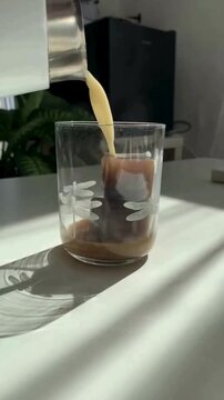 Hand Putting Frozen Coffee Cubes into Glass and Pouring Hot Milk for Aesthetic Iced Latte