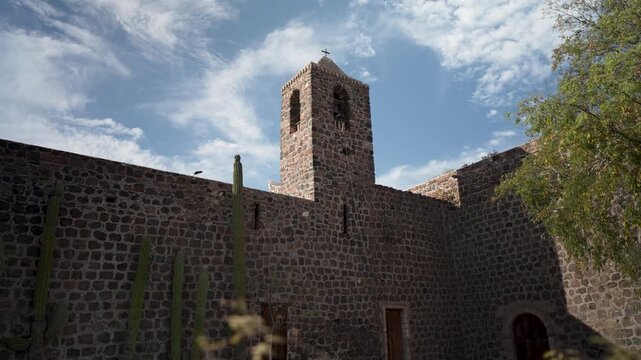 Discover Mission Church Santa Rosalia in Mulege Baja California, Mexico with palm trees and mountains in the background during a sunny day.