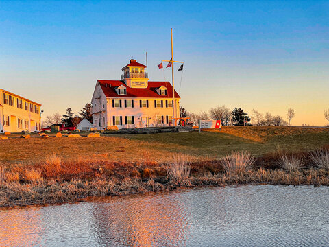 View of the US Coast Guard Station Martha's Vineyard with its distinctive red roof and white facade during golden hour across a calm pond in Edgartown, Massachusetts, United States.