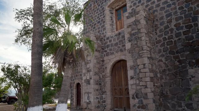 Mature woman visits the Mission Church of Santa Rosalia in Mulege, Baja California Sur, surrounded by lush palm trees and mountains. High quality 4k footage