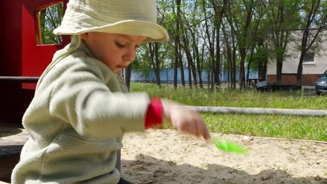 Child plays in sandbox with green shovel in sunny park