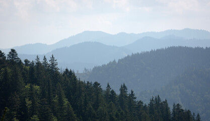 Naklejka premium Stunning view of layered mountains with lush green forests and soft clouds