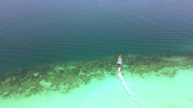 A longtail boat in a turqouse colored ocean with clear water at Koh Kradan, a tropical island in Trang, Thailand, and a coral reef in front of a tropical island