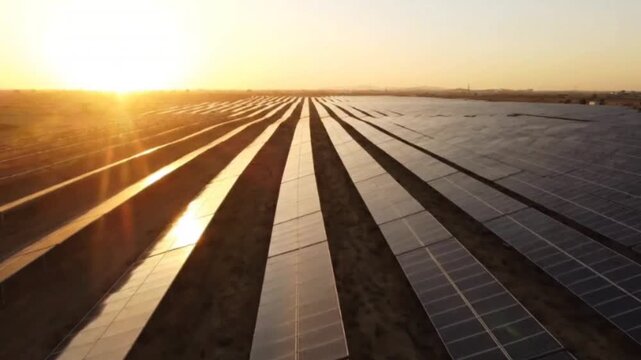Aerial view of large solar farm park in desert at sunset capturing rows of photovoltaic panels under glowing sky demonstrating sustainable energy power generation.