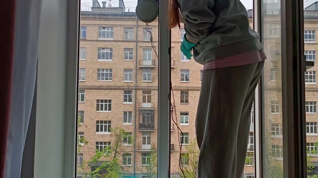 Woman cleaning large window with apartment buildings visible outside. professional cleaning, urban home maintenance.