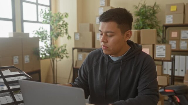Man with laptop leaning back with hands behind head in office building surrounded by cardboard parcels and packing shelves; relief productivity.