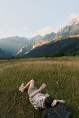 Fototapeta premium Young woman with short hair lies on grass in a mountain meadow enjoying a peaceful moment during a sunny day.