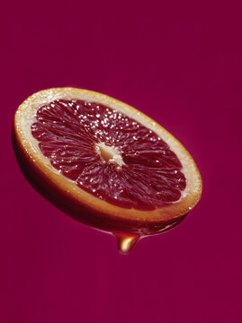 Half blood orange with a dripping juice droplet on a magenta background. Fresh citrus food concept for menu design, packaging, advertising and social media.