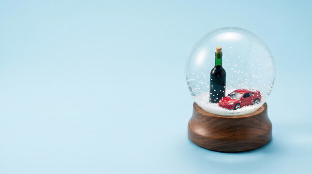 Red car and wine bottle inside a snow globe. Concept of drinking and driving awareness. Safety message about road accident prevention during holiday season travel and celebration.