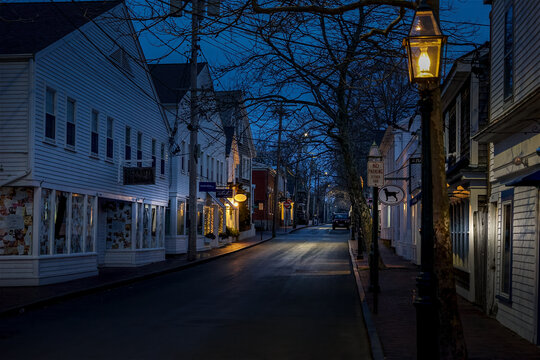View of Martha's Vineyard featuring historic white wooden buildings and glowing street lamps along a quiet street at twilight in Edgartown, Massachusetts, United States.
