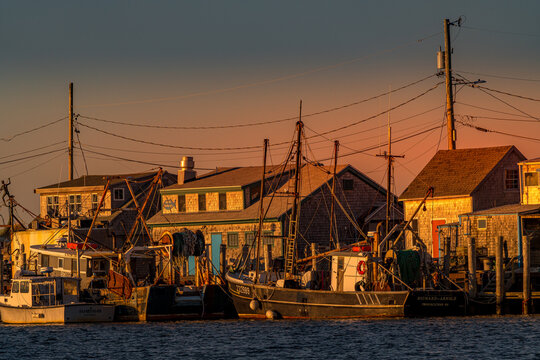 View of Martha's Vineyard with fishing boats docked at the harbor beside shingled buildings under a golden sunset sky in Edgartown, Massachusetts, United States.