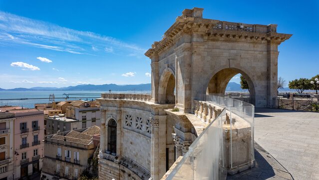 View of the Bastione di Saint Remy featuring its neoclassical stone arch and terrace overlooking city rooftops and the Mediterranean Sea in Cagliari, Sardegna, Italy.