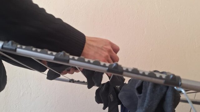 A hand picks up a pair of dried socks from a drying rack