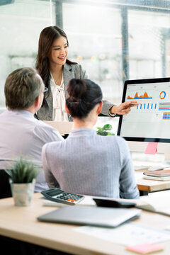 Asian Businesswoman Presenting Financial Data on Computer Screen to Team