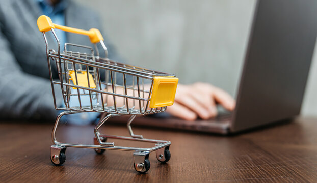 Close-up of empty shopping cart with laptop in background, showing e-commerce, online marketplace, abandoned cart, digital shopping and retail strategy.