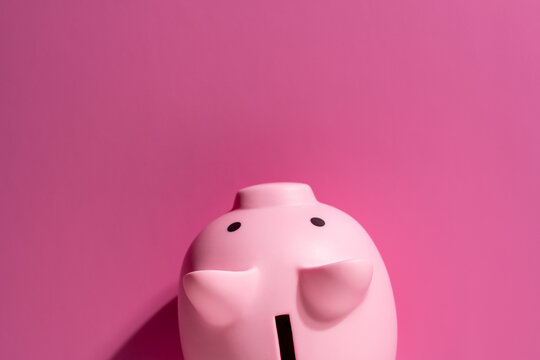 Top view of pink piggy bank on a matching pink background with ample copy space. Minimalist financial concept for savings budget bank deposits and money planning