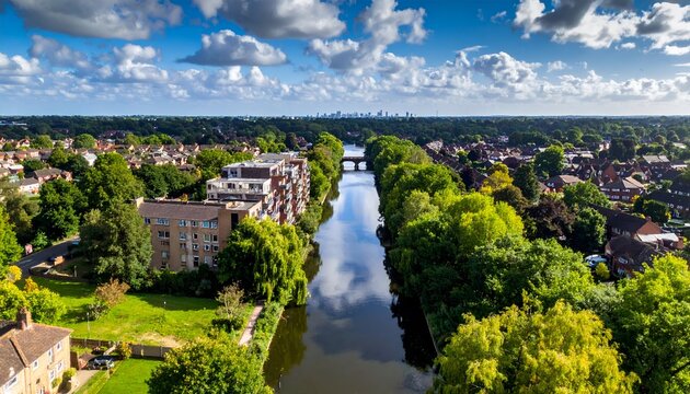 Canal lined by trees & buildings under partly cloudy sky, cityscape distant