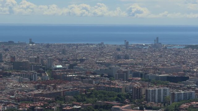 Barcelona skyline aerial view showing the dense city buildings, urban grid, and the vast mediterranean sea under a cloudy blue sky, capturing the iconic european cityscape