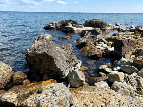 A wide-angle shot of a rugged rocky shore meeting the calm blue waters of the sea under a bright summer sky.