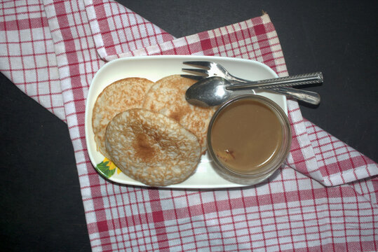 Traditional Indonesian serabi pancakes with sweet caramel palm sugar syrup served on plate and red checkered napkin.