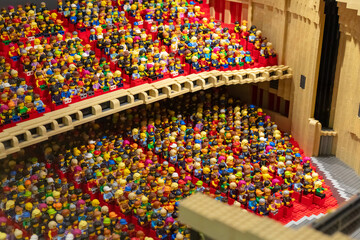 Obraz premium Many Lego figures sit closely together in a theater. They are watching a show. The seats are red, and the stage area shows wooden details. Selective Focus