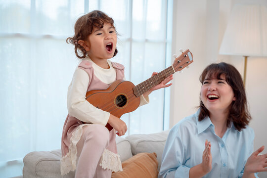 Little girl playing ukulele and singing passionately with her mother