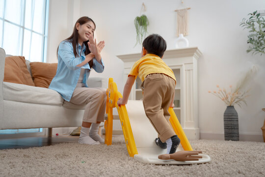 oyful little boy sliding down indoor playground with supportive mother