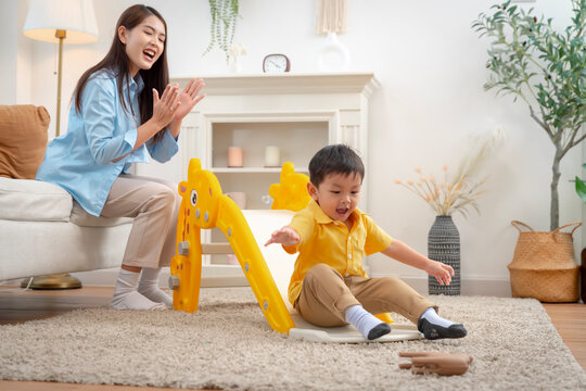 oyful little boy sliding down indoor playground with supportive mother